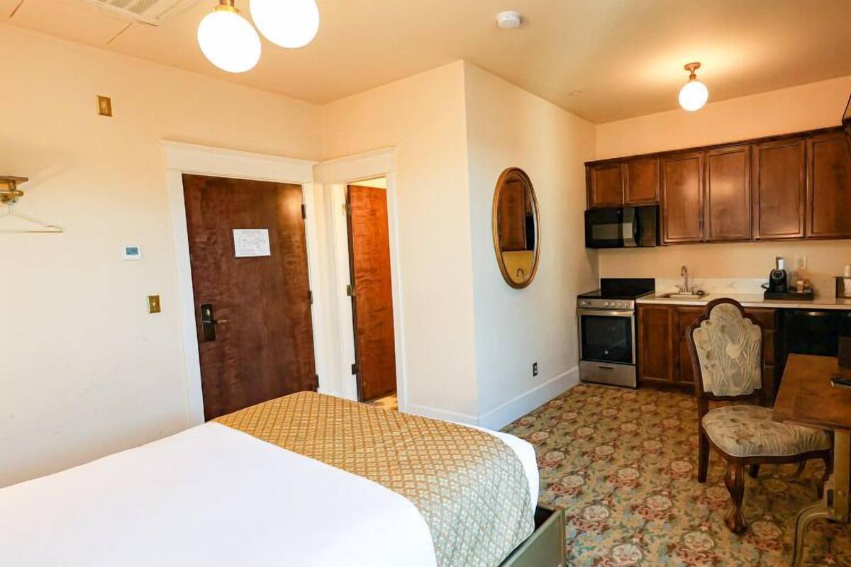 A hotel room with a bed, a chair, a small kitchen area with a microwave, and a sink.