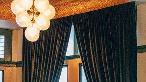 A room with a round table, four chairs, a lamp, and a window with curtains. - Belvada Hotel (Tonopah)