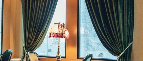Una habitación con una mesa redonda, cuatro sillas, una lámpara y vistas amplias a través de ventanas con cortinas.