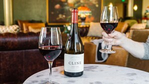 A bottle of Cline Pinot Noir wine and two glasses on a marble table in a cozy, well-lit room with a couch and a painting in the background. - Belvada Hotel (Tonopah)