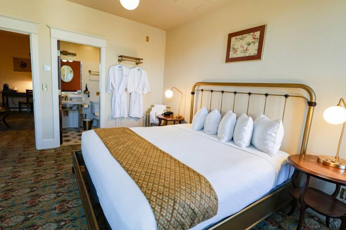 A hotel room with a large bed, bedside tables, a desk, and a bathroom visible through an open door.