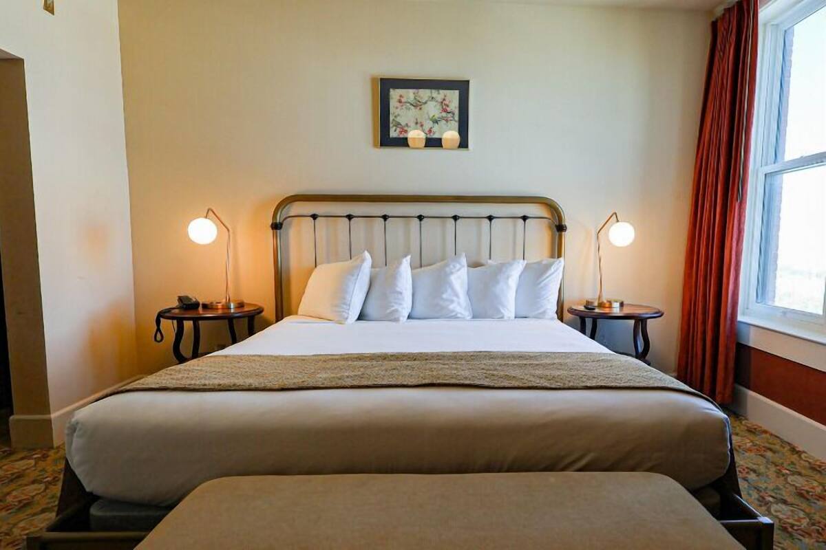 A double bed with a metal headboard, two bedside tables with lamps, a framed artwork above the bed, and a window with curtains.
