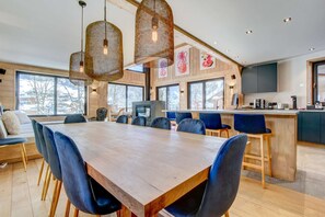 A modern kitchen with a wooden dining table, blue chairs, and hanging pendant lights.