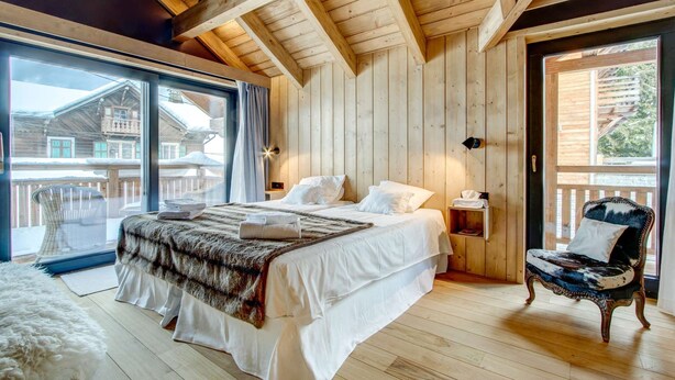 A wooden-paneled bedroom with a large bed, a chair, and a view of a wooden building outside. - Nosefosa - Stunning new chalet with inside swimming pool (MORZINE)