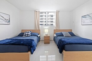 A modern bedroom with two beds, a nightstand, a window with curtains, and artwork on the walls.