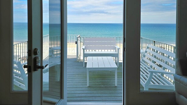 A view from a room with a door leading to a balcony overlooking a beach.