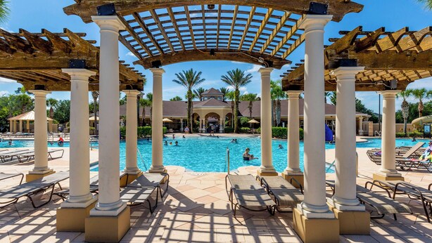 A pool area with a pergola structure, lounge chairs, and a clear blue sky.