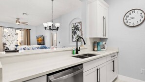 A kitchen with a white countertop, a sink, a dishwasher, a coffee maker, and a clock on the wall.