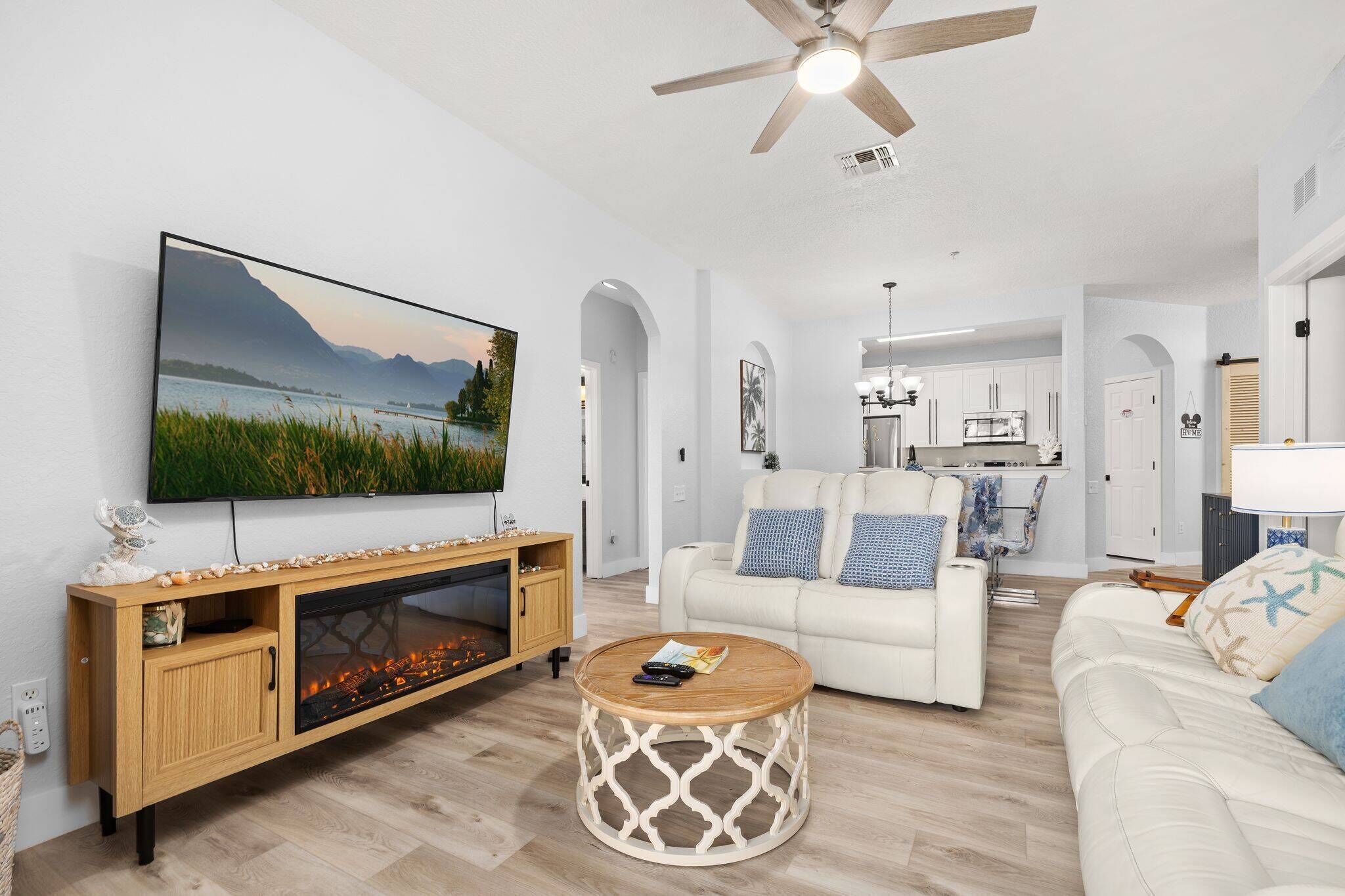 Een moderne woonkamer met een flatscreen televisie, een open haard, een ronde salontafel en een witte bank.