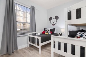 A child's room with a bunk bed, a Mickey Mouse wall decal, and a window with blinds. - Windsor Hills Dream - 3BR - 2 miles from Disney! (Kissimmee)
