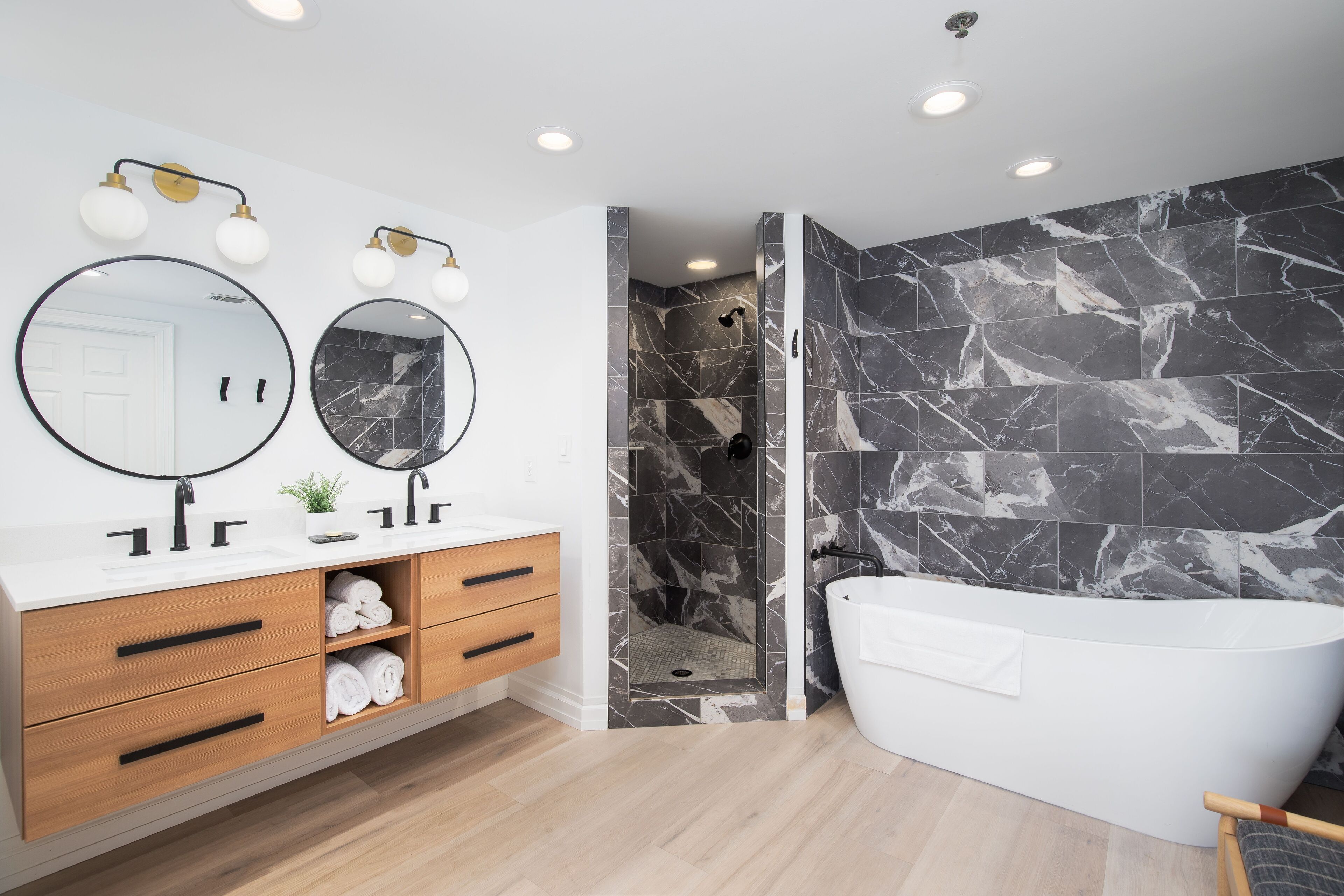 Une salle de bain moderne avec un meuble-lavabo blanc, deux miroirs ronds, une baignoire et un espace douche aux carreaux de marbre.