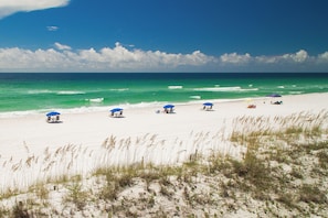 Une plage de sable blanc, avec une eau turquoise et limpide, et quelques parasols.