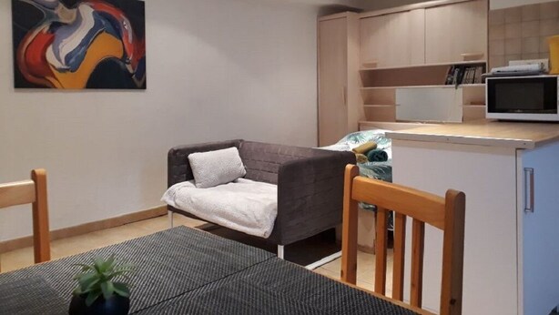 Un espacio habitable compacto con kitchenette, un sofá, una mesa de comedor y un cuadro en la pared.