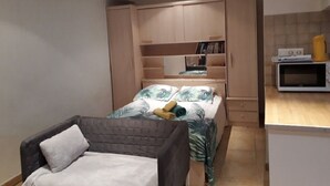 Una habitación compacta con cama, un pequeño sofá, armario y una zona de kitchenette.
