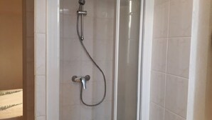 Una ducha con cerramiento de vidrio, cabezal de ducha de mano y grifo empotrado en la pared.