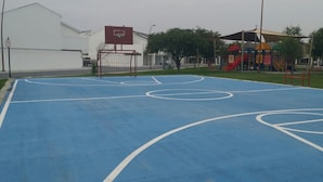 An outdoor basketball court with a basketball hoop and a playground with slides in the background. - RAGOL 502 ALMERIA MONTERREY MINUTOS DE AEROPUERTO (ALMERIA)