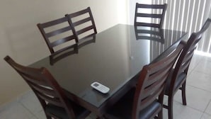 A dining table with four wooden chairs, a digital device on the table, and a window with blinds in the background. - RAGOL 502 ALMERIA MONTERREY MINUTOS DE AEROPUERTO (ALMERIA)