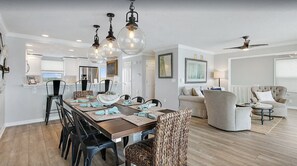 A spacious dining area with a wooden table and chairs, a kitchen in the background, and a living room with a sofa and armchairs.
