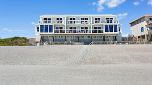 Ein mehrstöckiges Gebäude direkt am Strand mit Balkonen, großen Fenstern und einem Sandstrand im Vordergrund.