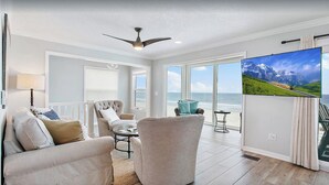Ein geräumiges Wohnzimmer mit großem Fernseher, bequemen Sitzgelegenheiten und Meerblick.