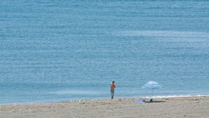 Ein Strand mit einer Person in der Nähe des Wassers, einem Sonnenschirm und einigen Strandgegenständen.