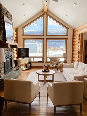 A cozy living room with a fireplace, large windows, and a stone wall.