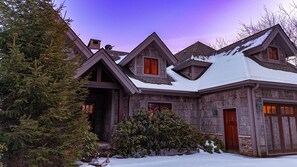 Uma grande casa de pedra com vários andares, telhado coberto de neve e várias chaminés.