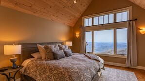 Ein Schlafzimmer mit einem großen Bett, Holzboden, einem Fenster mit Aussicht und zwei Nachttischlampen.