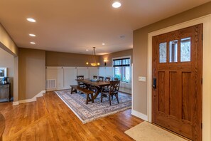 A dining area with a wooden table and chairs, a hanging light fixture, and a large wooden door.