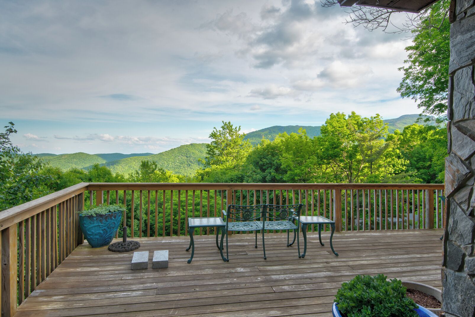 A wooden deck with a view of green hills and a cloudy sky.