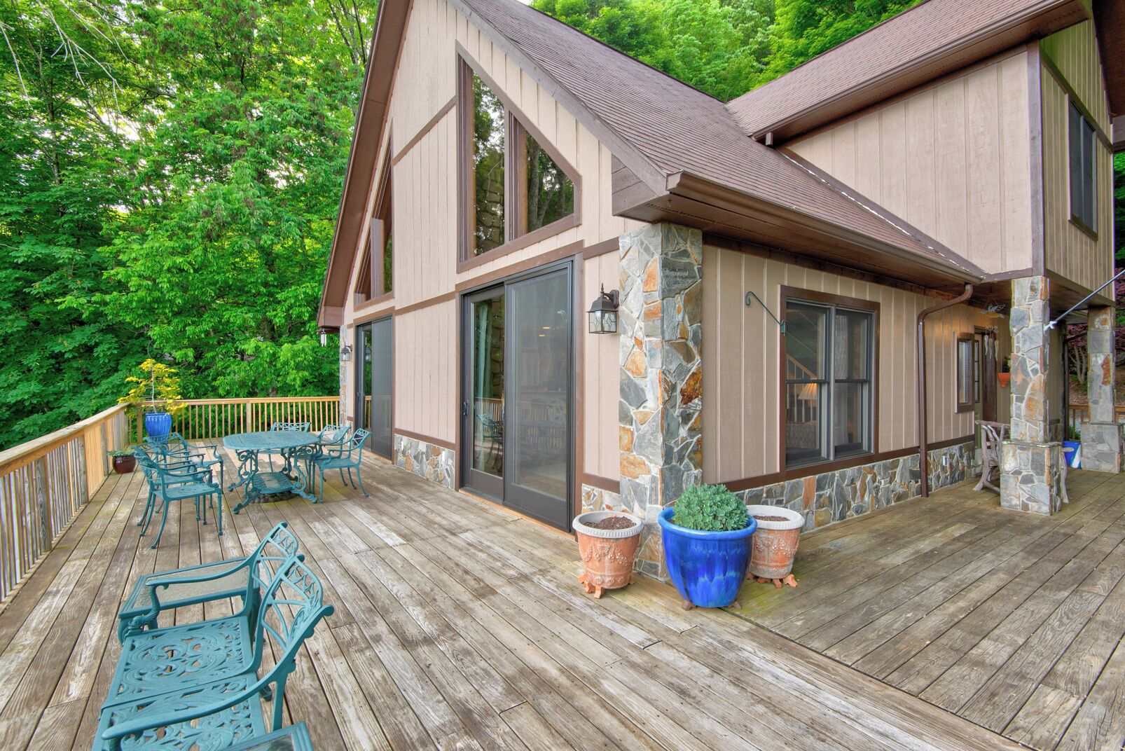 A wooden deck with outdoor furniture, stone accents, and a view of lush greenery.