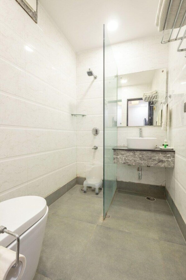 A bathroom with a glass shower enclosure, a white toilet, a marble sink, and a mirror above the sink. - Cosmo Hotel (New Delhi)