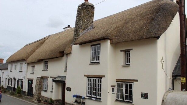 A row of traditional buildings with thatched roofs and white walls, featuring a small outdoor seating area with tables and chairs.