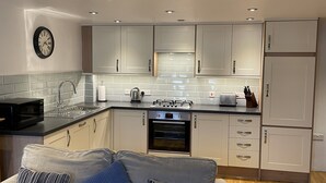 A modern kitchen with white cabinets, a black countertop, a microwave, a kettle, a toaster, and a refrigerator.