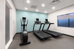 A fitness room with treadmills and an elliptical machine, carpeted floor, and a window with blinds. - Tru by Hilton Portland Airport (Portland)