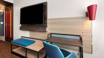 Een moderne kamer met een aan de muur bevestigde televisie, een houten bureau, een blauwe zachte bank en een rode lamp.