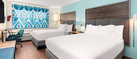 A hotel room with two beds, a desk, a chair, and a large window with a blue and white patterned wall.