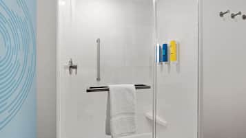 A modern shower area with a glass door, a white towel hanging on a rack, and toiletries on a shelf.