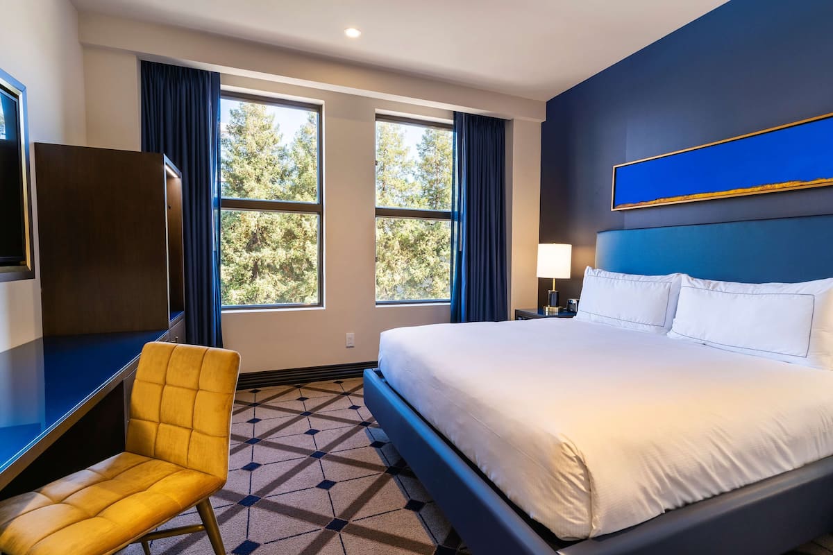 A hotel room with a large bed, a desk, a chair, and a window with curtains.