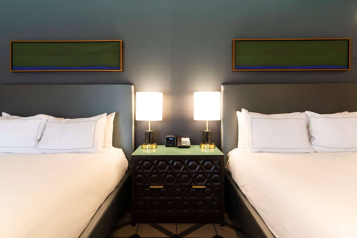 A hotel room with two beds, a nightstand with lamps, a phone, and a clock.