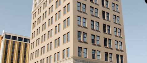 A tall, beige building with a symmetrical facade, large windows, and a prominent entrance with a canopy.