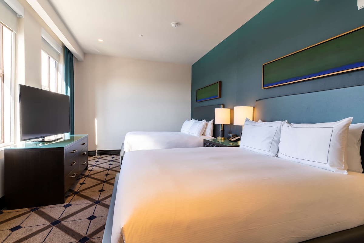 A hotel room with two beds, a TV, a desk, and a lamp.