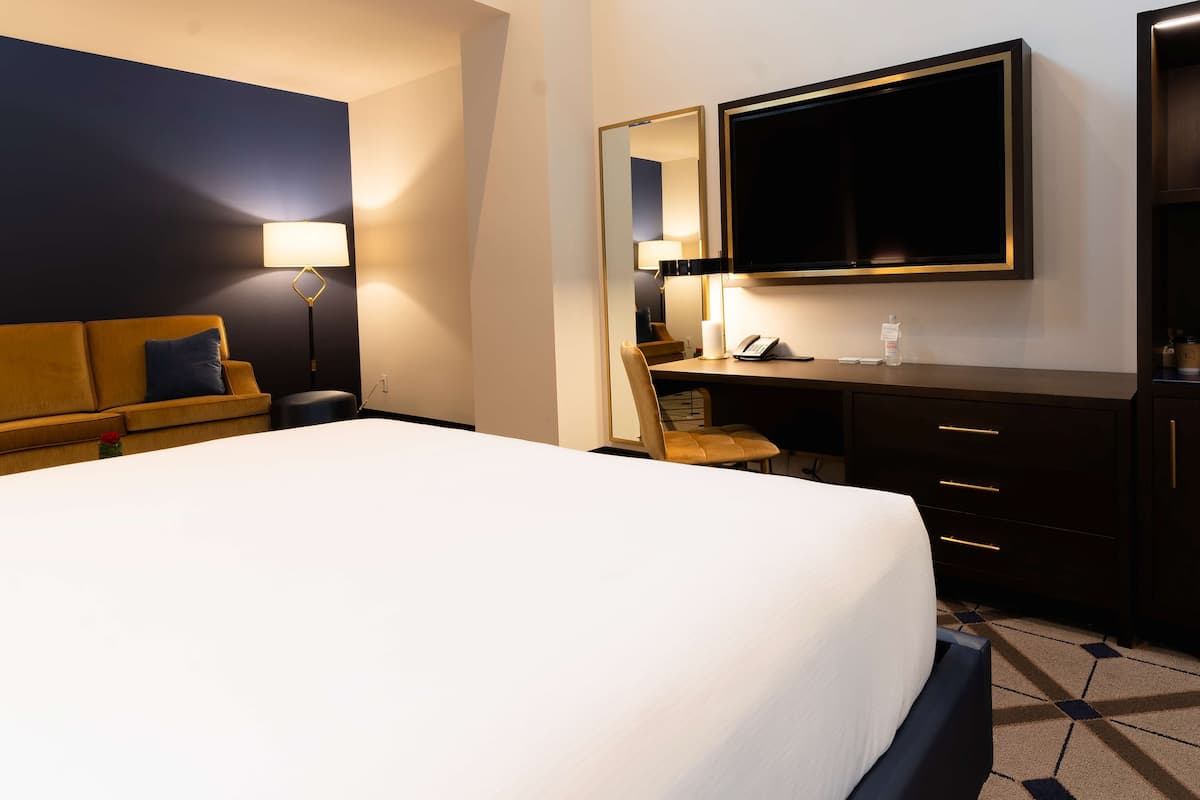 A hotel room with a large bed, a desk with a chair, a television, and a sofa.