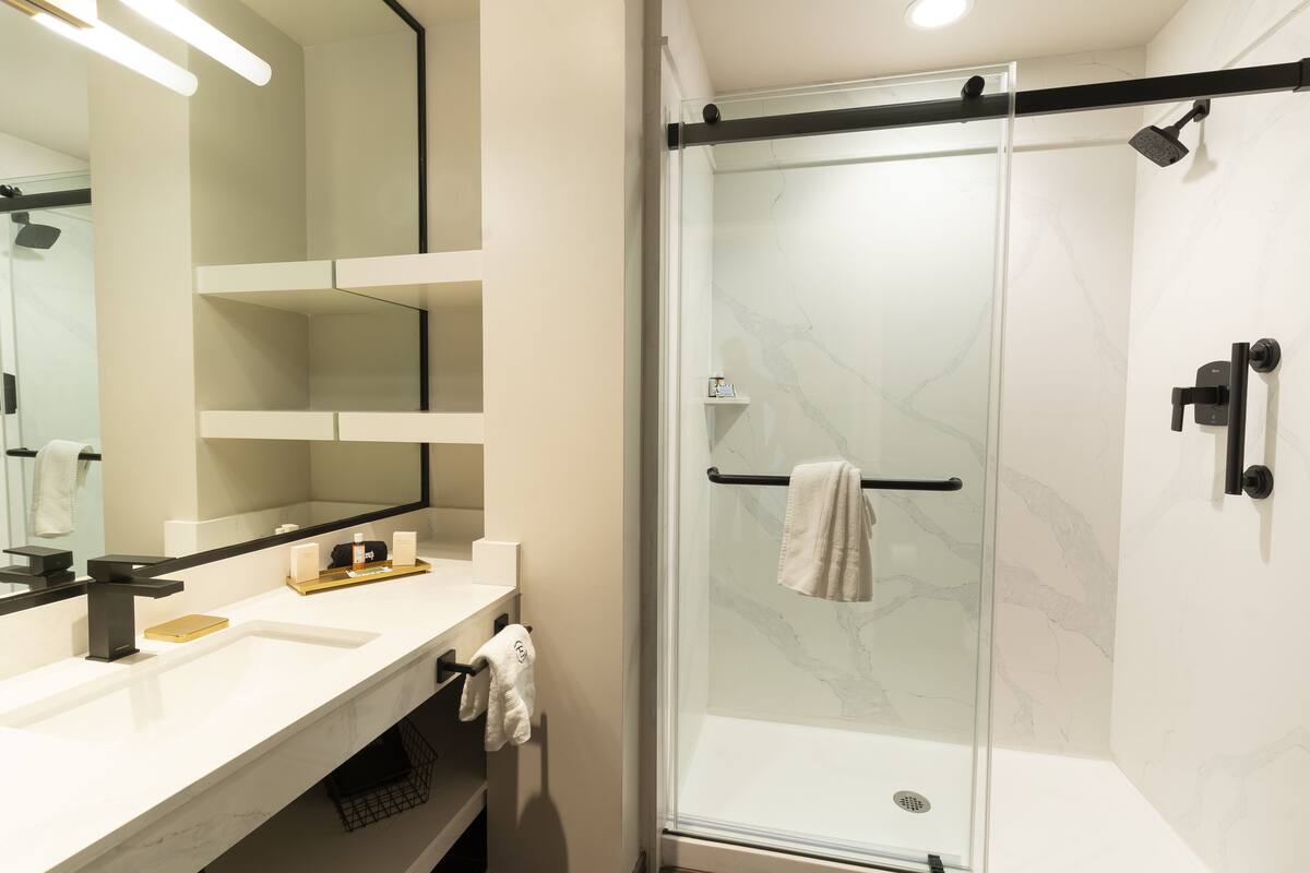 A modern bathroom with a glass-enclosed shower, a white sink, and a large mirror.