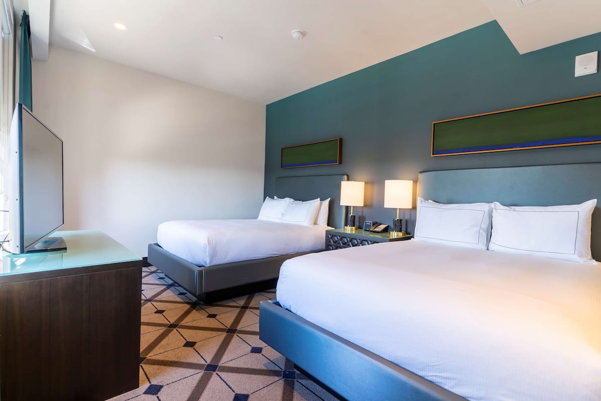 A hotel room with two beds, a desk, and a TV.