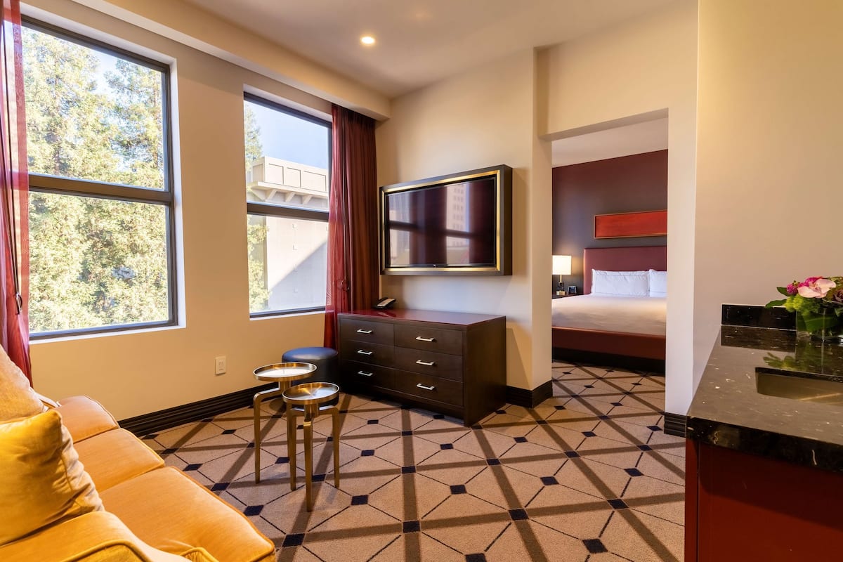 A hotel room with a sofa, a TV, a bed, a dresser, and a bathroom with a sink and mirror.