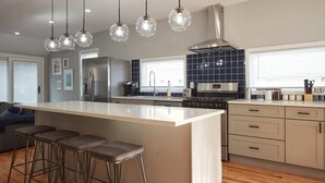 Une cuisine moderne dotée d’un îlot central, de tabourets de bar, d’appareils électroménagers en acier inoxydable et de luminaires suspendus.