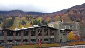 Un bâtiment avec un télésiège en arrière-plan, entouré d’arbres aux couleurs automnales et de montagnes.