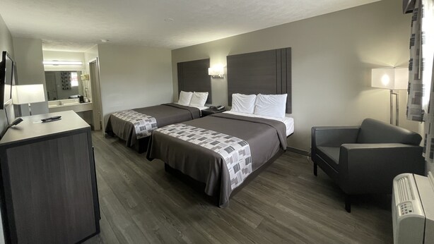 A hotel room with two beds, a desk, a chair, and a TV. - Embassy Inn (Hohenwald)