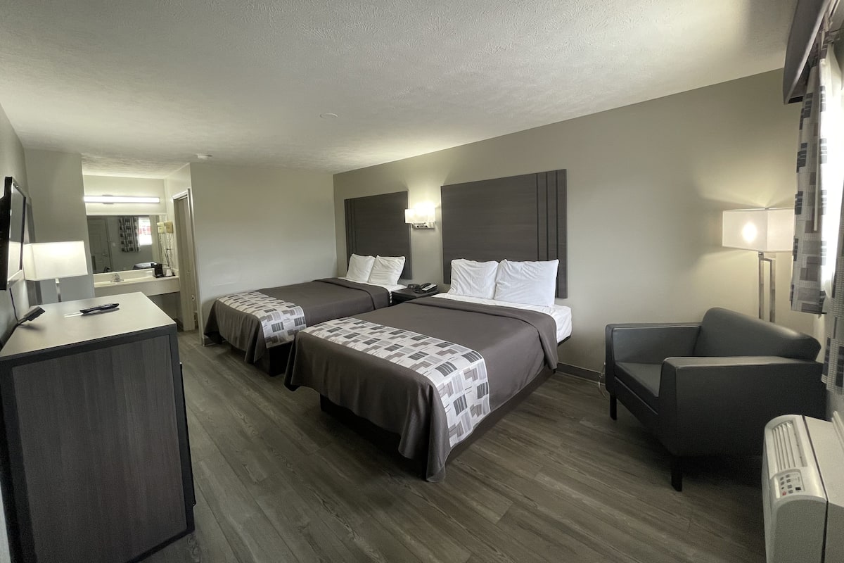 A hotel room with two beds, a desk, a chair, and a TV.